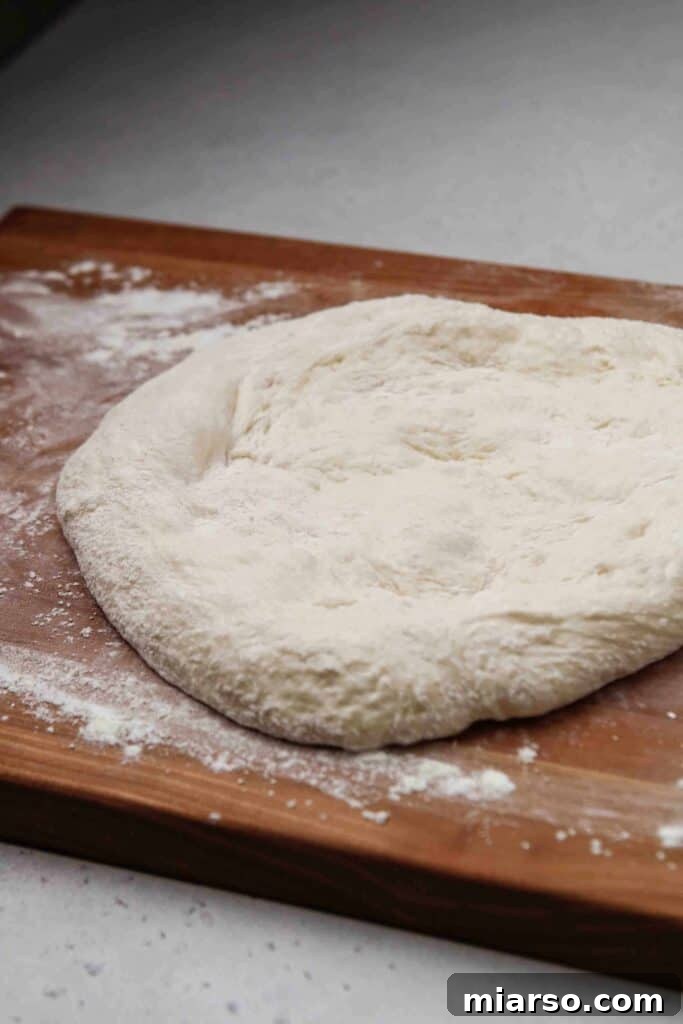 Flattening the risen pizza dough on a well-floured surface with hands.
