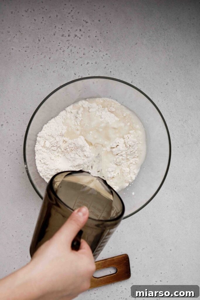 Adding lukewarm water to the flour and yeast mixture in a bowl.