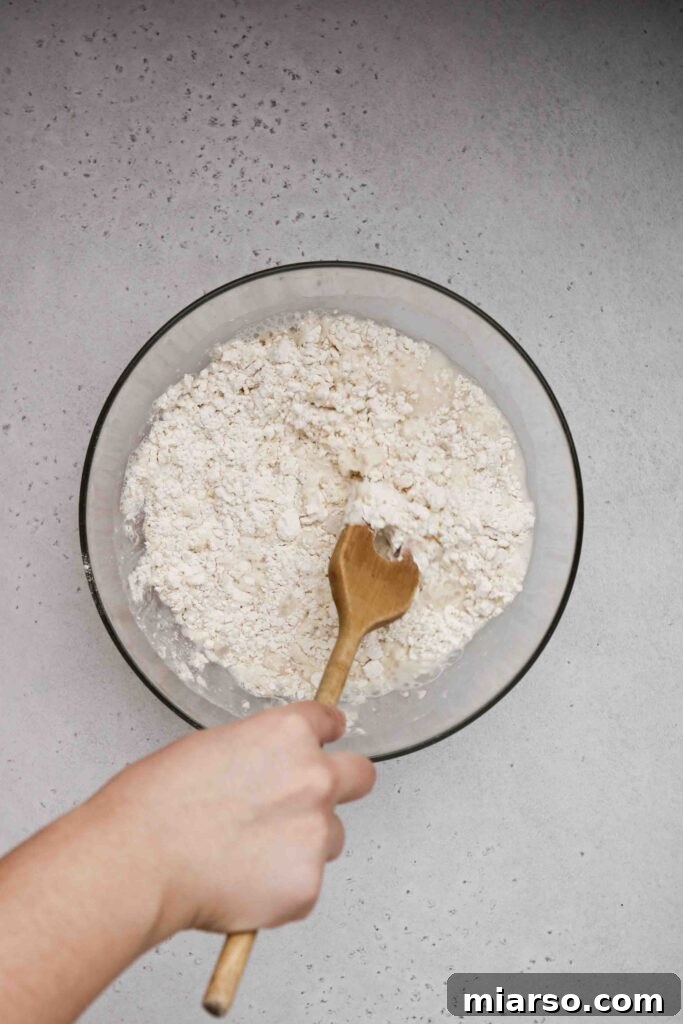 Mixing the sticky pizza dough with a wooden spoon until well combined.