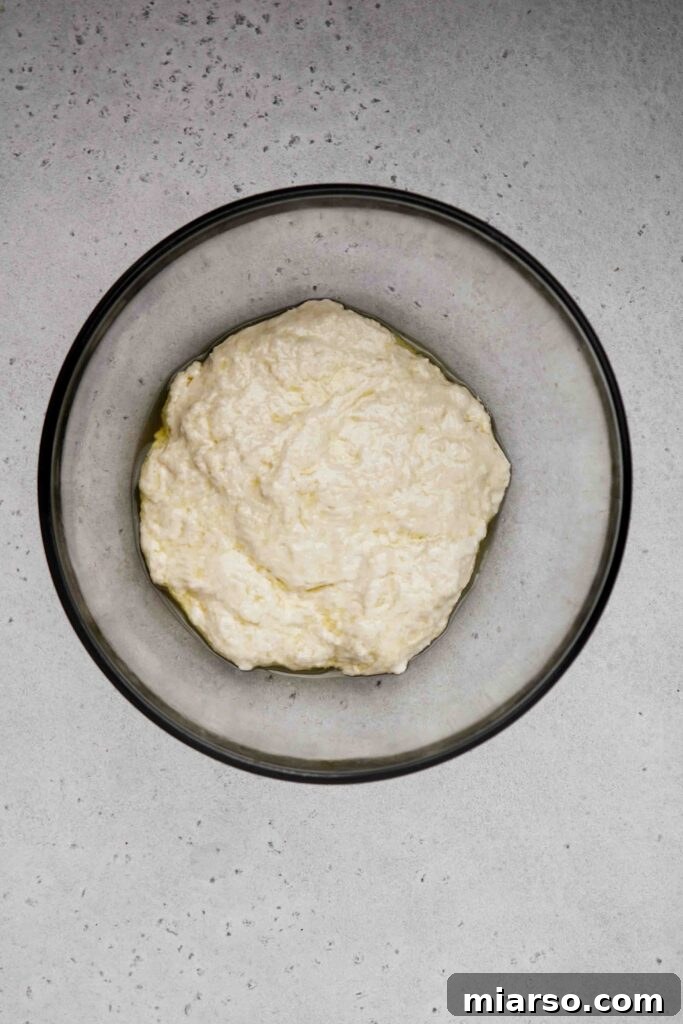 Coating the pizza dough with olive oil in a bowl before rising.