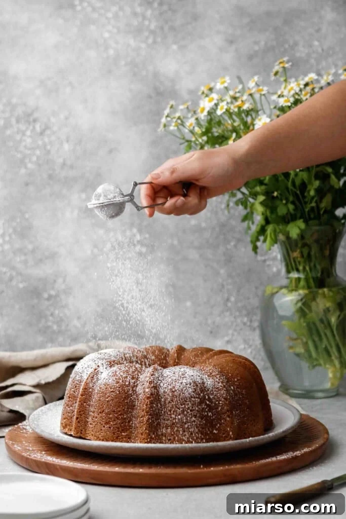 Velvety Vanilla Bundt Perfection 13 Dusting powdered sugar on cake