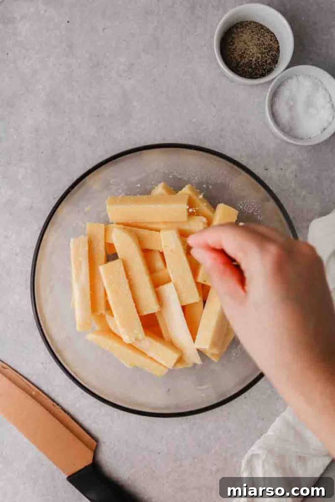 Polenta fries seasoned with salt and pepper in a bowl before air frying