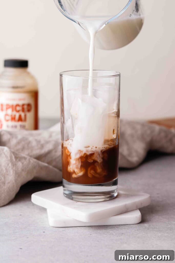 Adding milk to a glass with chai concentrate and ice