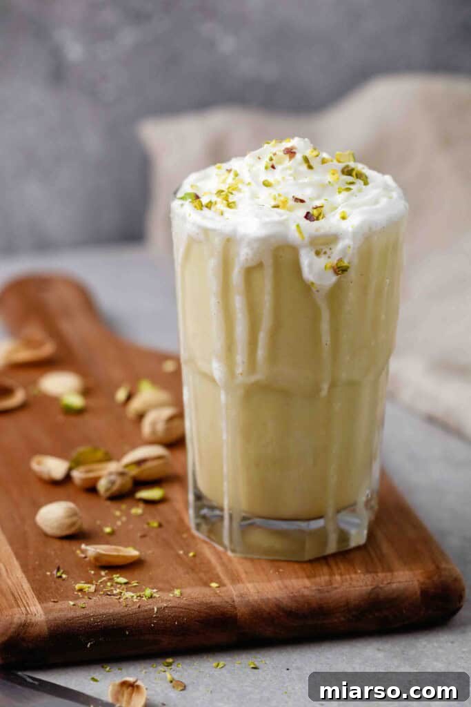 A beautifully presented Starbucks pistachio frappuccino copycat recipe on a rustic cutting board, adorned with whipped cream and a sprinkle of chopped pistachios, ready to be enjoyed.