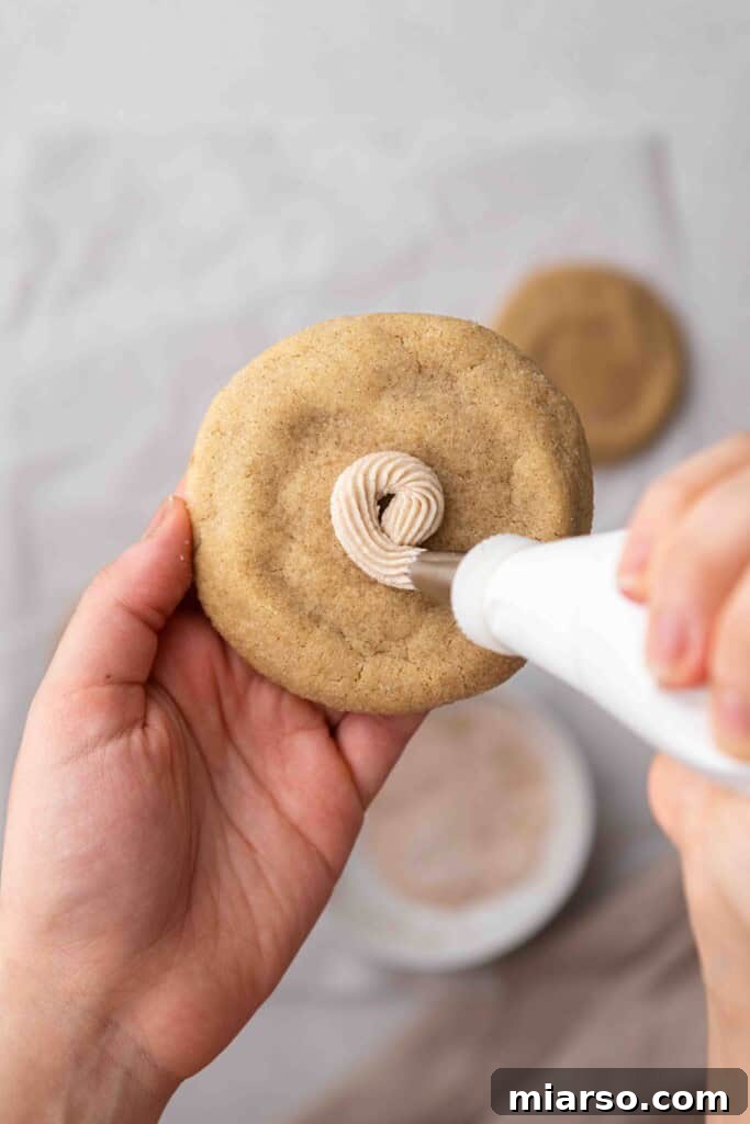A hand expertly piping cinnamon buttercream onto a cooled churro cookie.