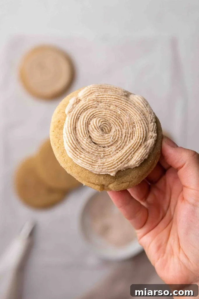 A hand proudly holding a finished copycat Crumbl Churro Cookie, showcasing its delicious frosting and cinnamon sugar.