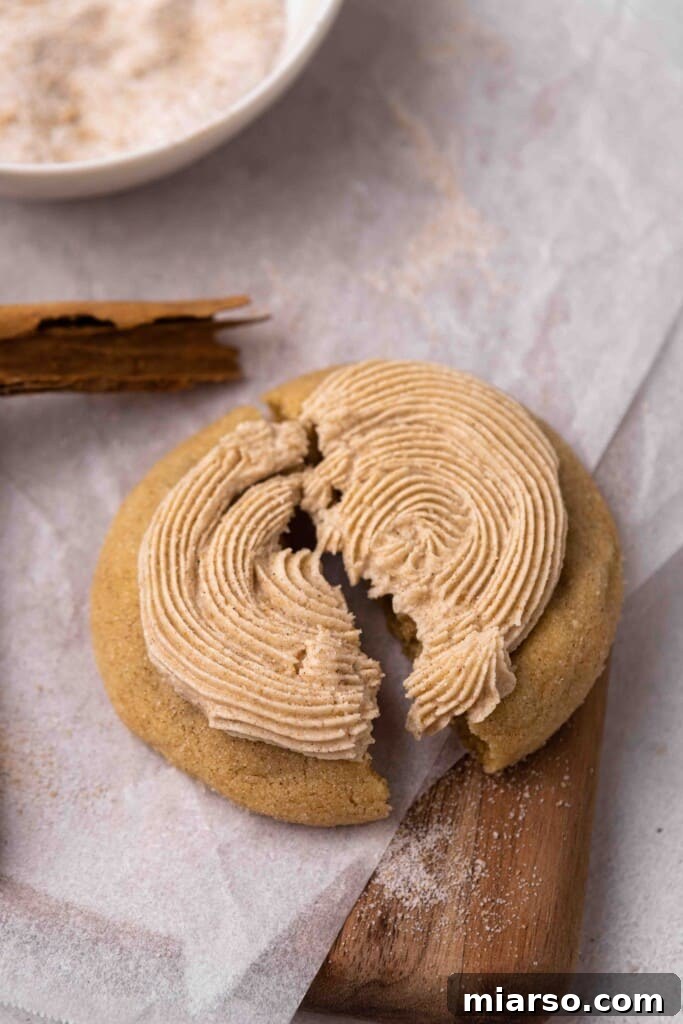 A frosted cinnamon churro cookie beautifully broken in half, revealing its tender, chewy interior and creamy filling.