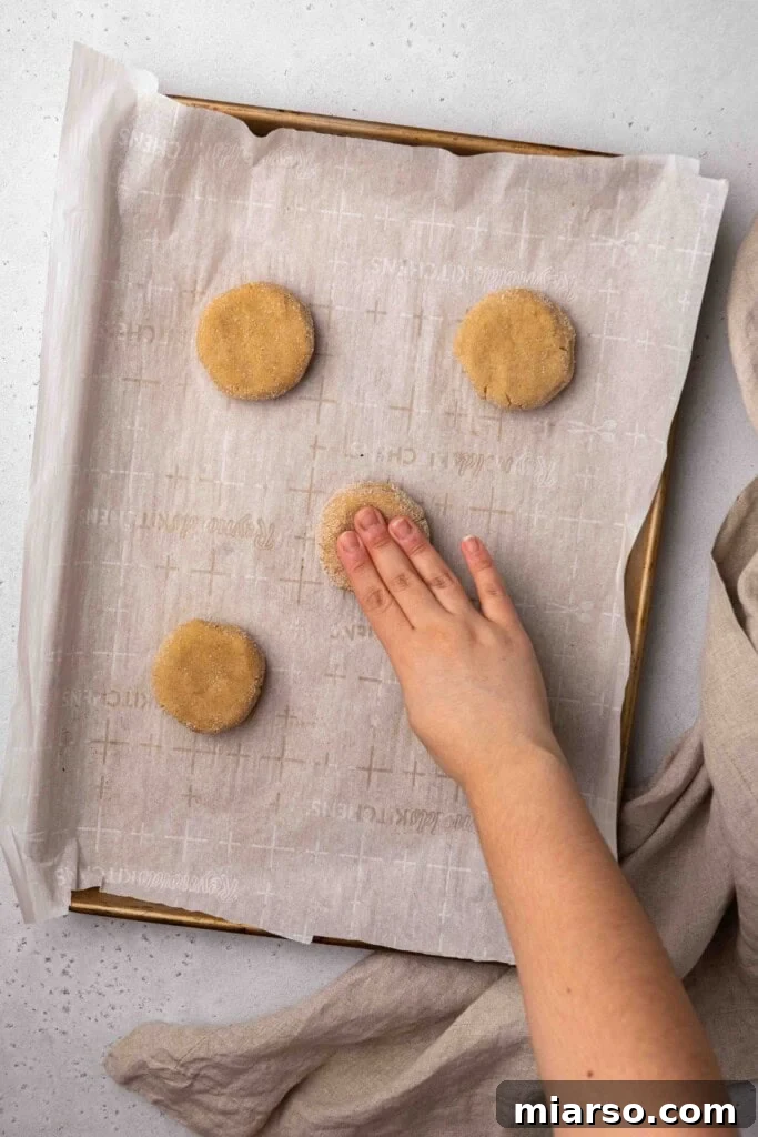 A hand gently flattening churro cookie dough balls before baking for even cooking.