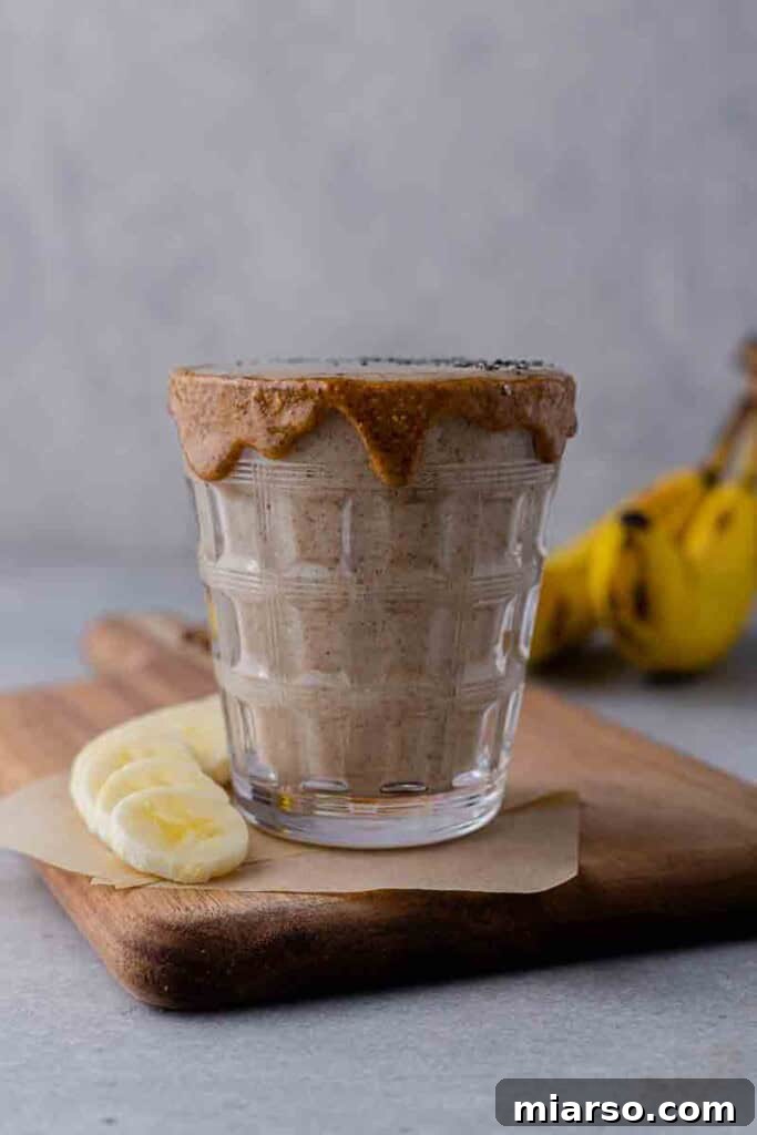 Creamy almond butter smoothie in a glass with a straw, garnished with almonds and a date