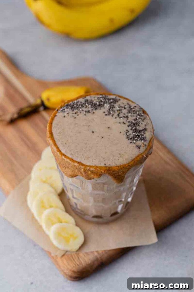 Close-up, 45-degree angle shot of the almond banana date smoothie in a glass, with dates and almonds scattered around