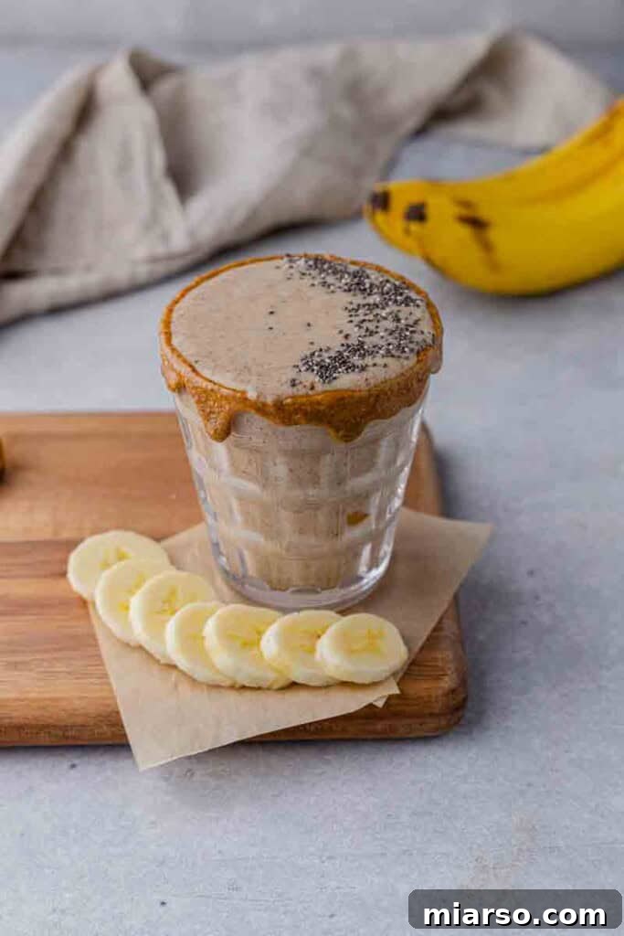 Easy banana smoothie in a tall glass with a straw, placed on a light wooden surface