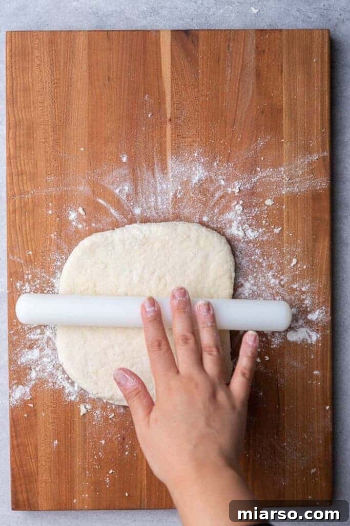 Hands gently rolling biscuit dough to an even thickness on a floured surface.