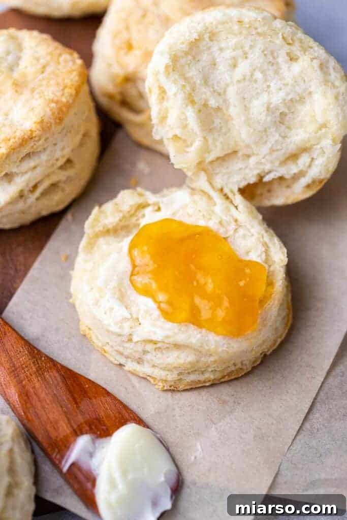 A warm, flaky homemade biscuit generously topped with vibrant red jam, ready to be enjoyed.
