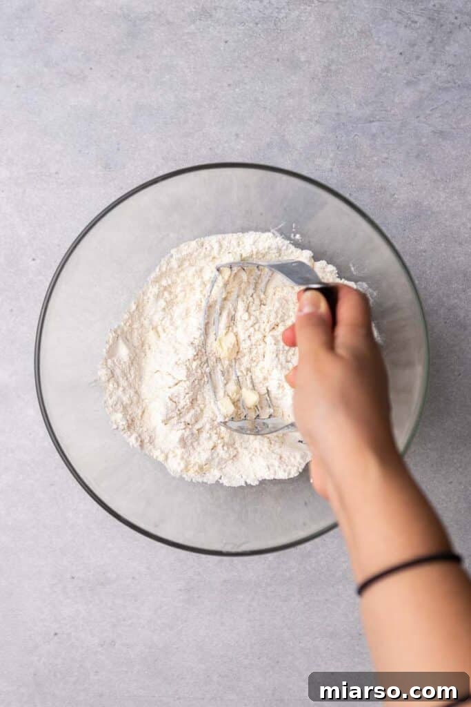 A pastry cutter being used to cut cold butter into the dry flour mixture.