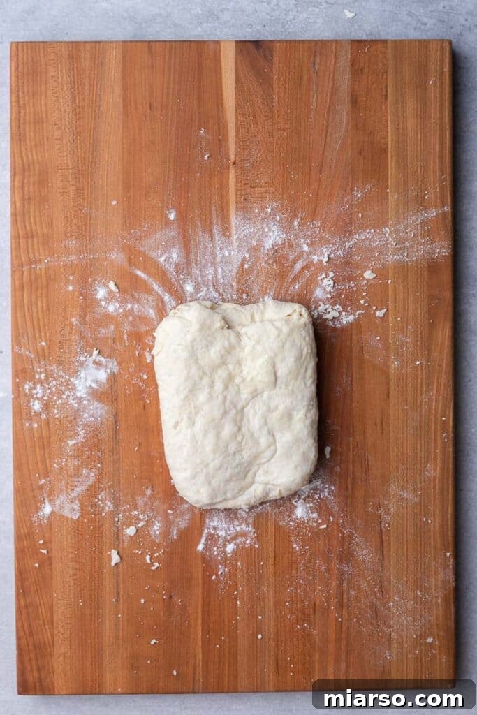 Biscuit dough being folded over itself to create layers, visible butter chunks still present.