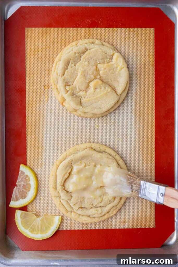 Effortless Crumbl Lemon Glazed Cookies 12 Applying lemon glaze to a cooled lemon cookie with a pastry brush.