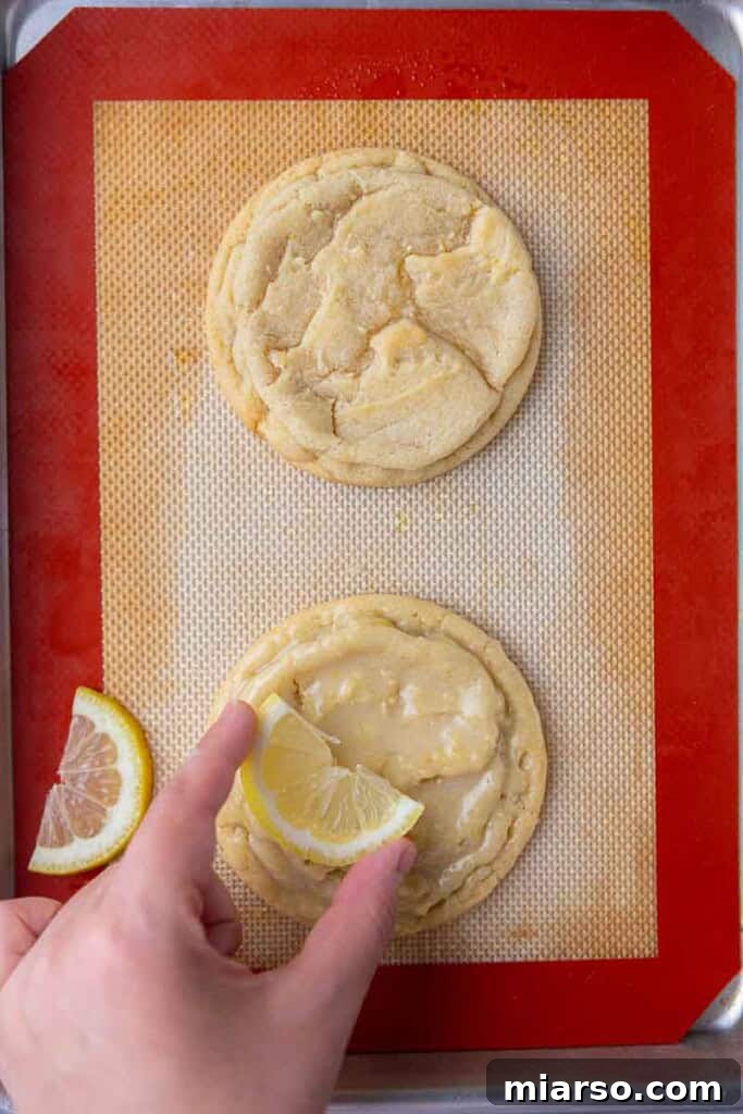 Effortless Crumbl Lemon Glazed Cookies 13 A hand placing a thin lemon slice on top of a glazed lemon cookie.