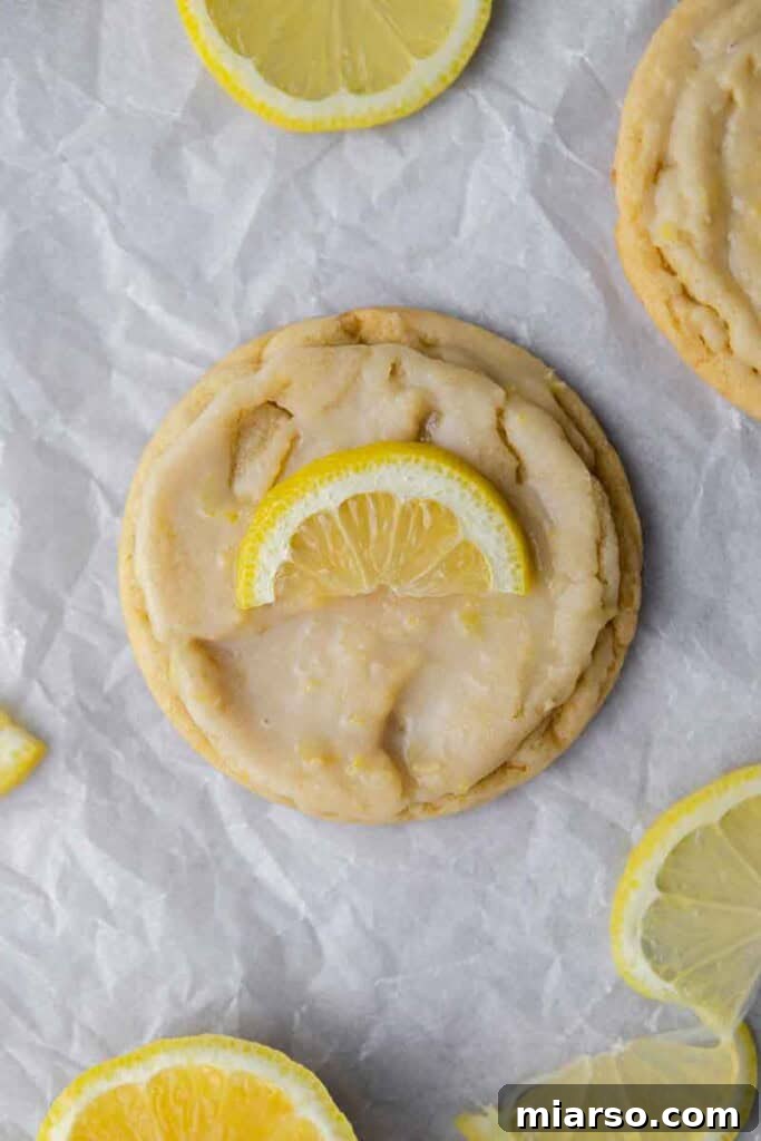 Effortless Crumbl Lemon Glazed Cookies 16 Overhead close-up of a stack of glazed CRUMBL Lemon Glaze cookies with fresh lemon slices.