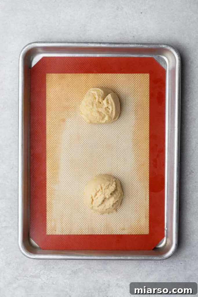 Effortless Crumbl Lemon Glazed Cookies 8 Scooped lemon cookie dough balls arranged on a parchment-lined baking sheet.