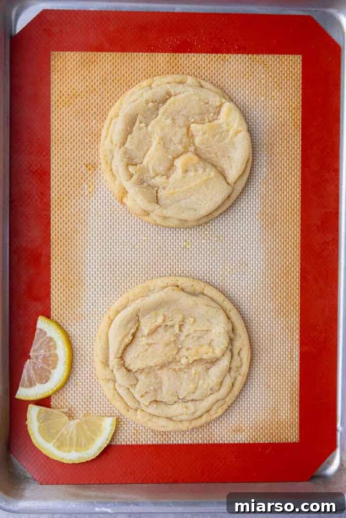 Effortless Crumbl Lemon Glazed Cookies 9 Freshly baked and rounded CRUMBL lemon glaze cookies on a baking sheet.