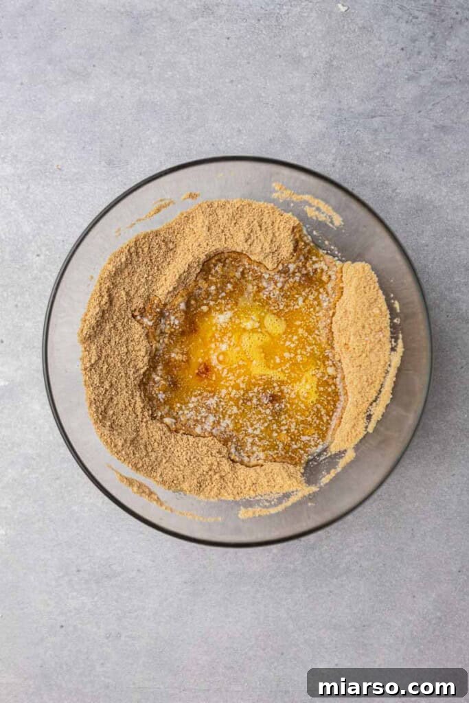 Close-up of graham cracker crumbs being mixed with butter, illustrating the first step of creating the cookie base.