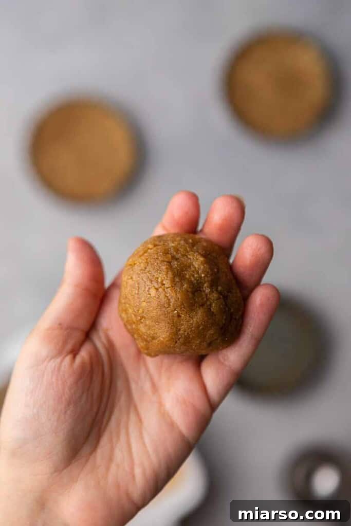 A hand holding a perfectly rounded cookie dough ball, showcasing its readiness for the next step.