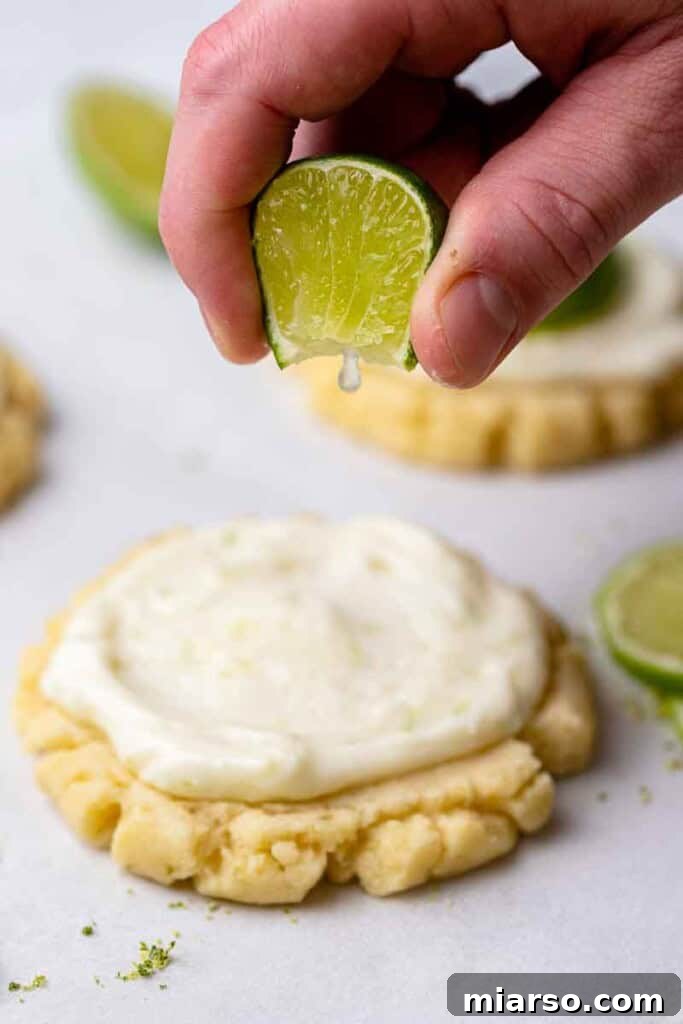 Hand squeezing fresh lime over frosted cookies