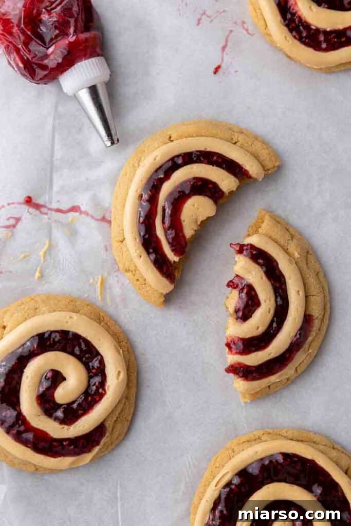 Soft Baked Peanut Butter and Jelly Cookies 13 A peanut butter and jelly cookie broken in half, revealing the jam and thick cookie.