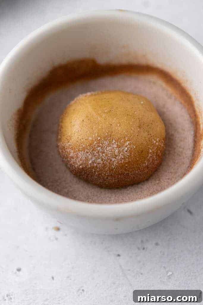 A single cookie dough ball being rolled in cinnamon sugar mixture