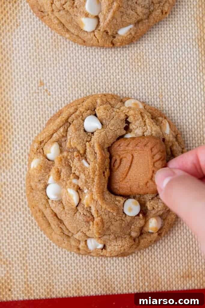 The Best Crumbl Biscoff White Chip Cookies Recipe 11 Hands carefully placing half a Biscoff cookie on top of a freshly baked cookie butter cookie, adding the finishing touch.