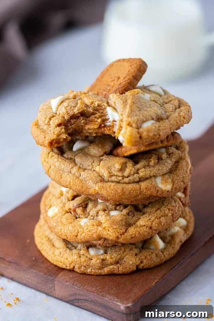 The Best Crumbl Biscoff White Chip Cookies Recipe 13 A stack of golden brown cookies, with one cookie having a bite taken out, revealing its soft, chewy interior.