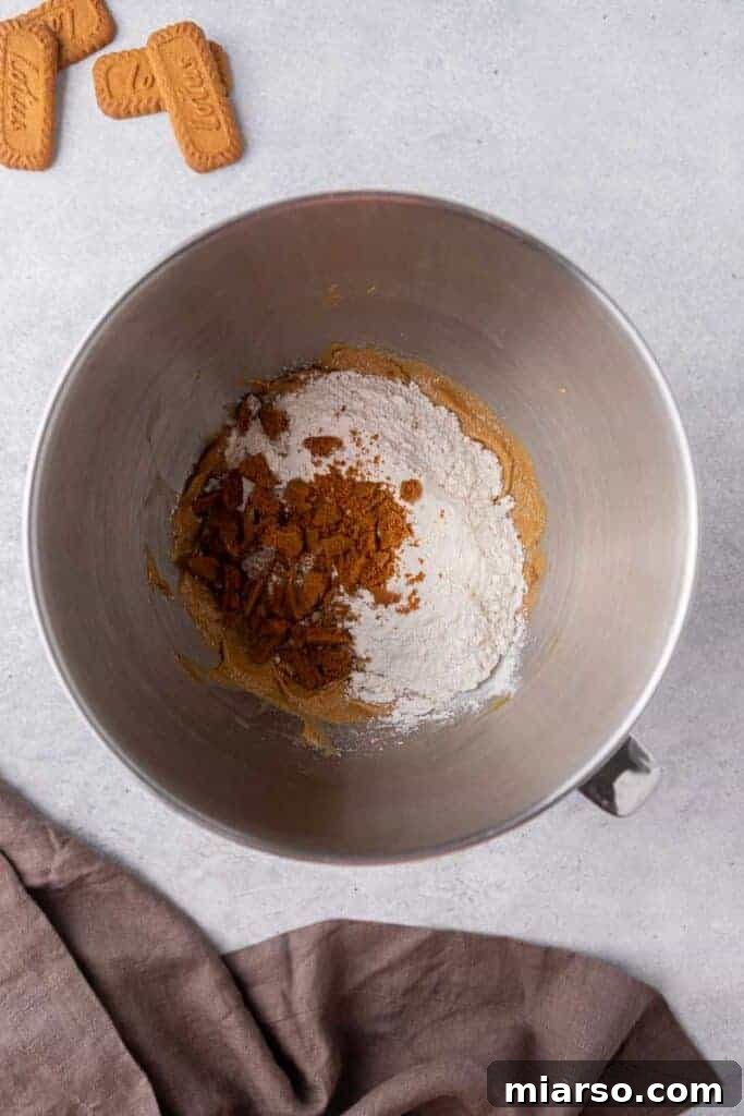 The Best Crumbl Biscoff White Chip Cookies Recipe 7 Dry ingredients mixed into the creamed butter and egg mixture in a bowl, illustrating the combining step of the cookie dough.