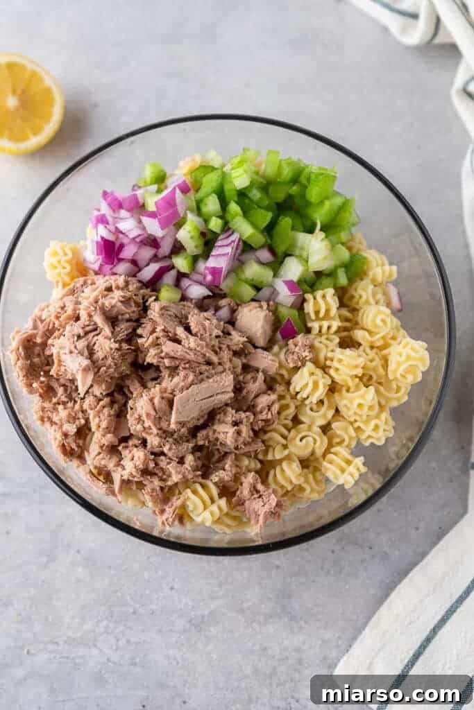 Cooked pasta, tuna, onions, and celery combined in a large mixing bowl