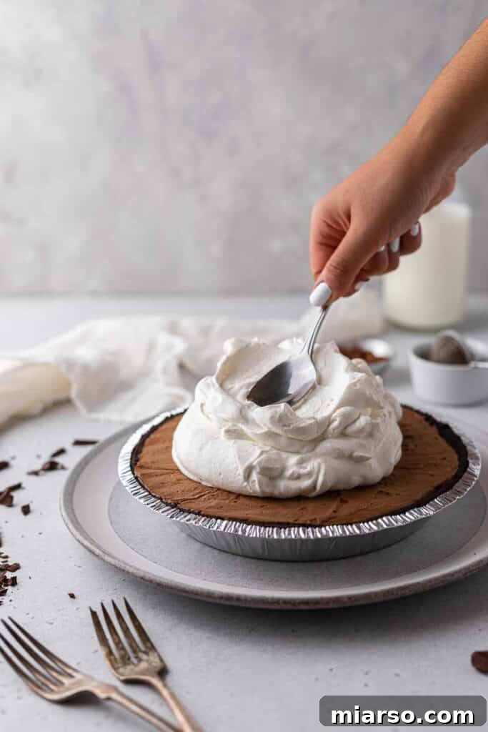 Decorating the chilled chocolate pie with a generous layer of freshly whipped cream.