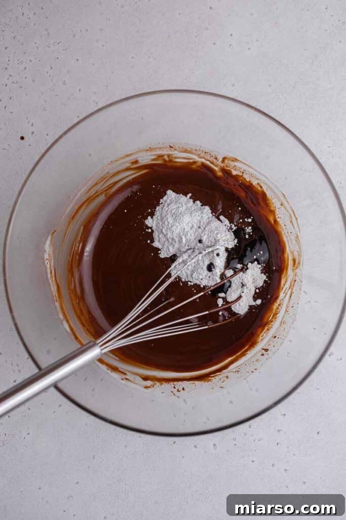 Adding powdered sugar, vanilla, and instant coffee to the cooled chocolate ganache for enhanced flavor.