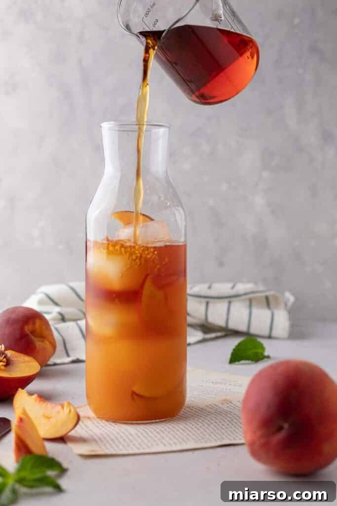 Combining the chilled peach syrup with black tea in a large pitcher, stirring for an even blend.