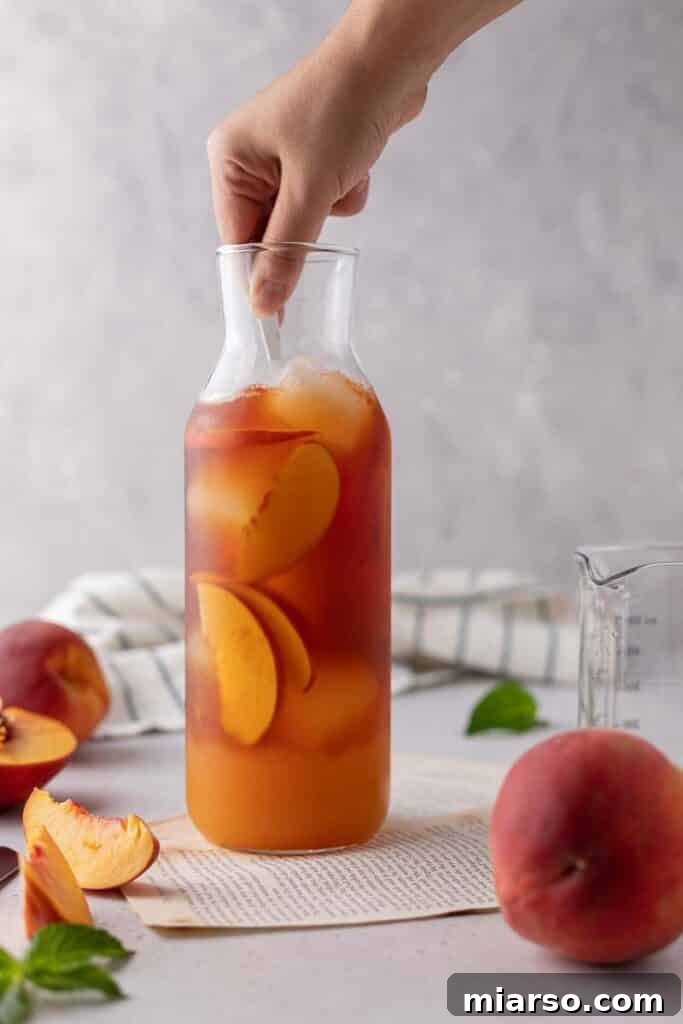The finished peach iced tea in a pitcher, garnished with fresh peach slices, ready to be served over ice.