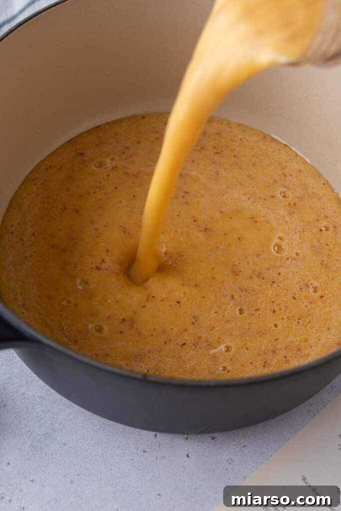 Pouring the blended peach mixture into a pot, ready for simmering to create the syrup.