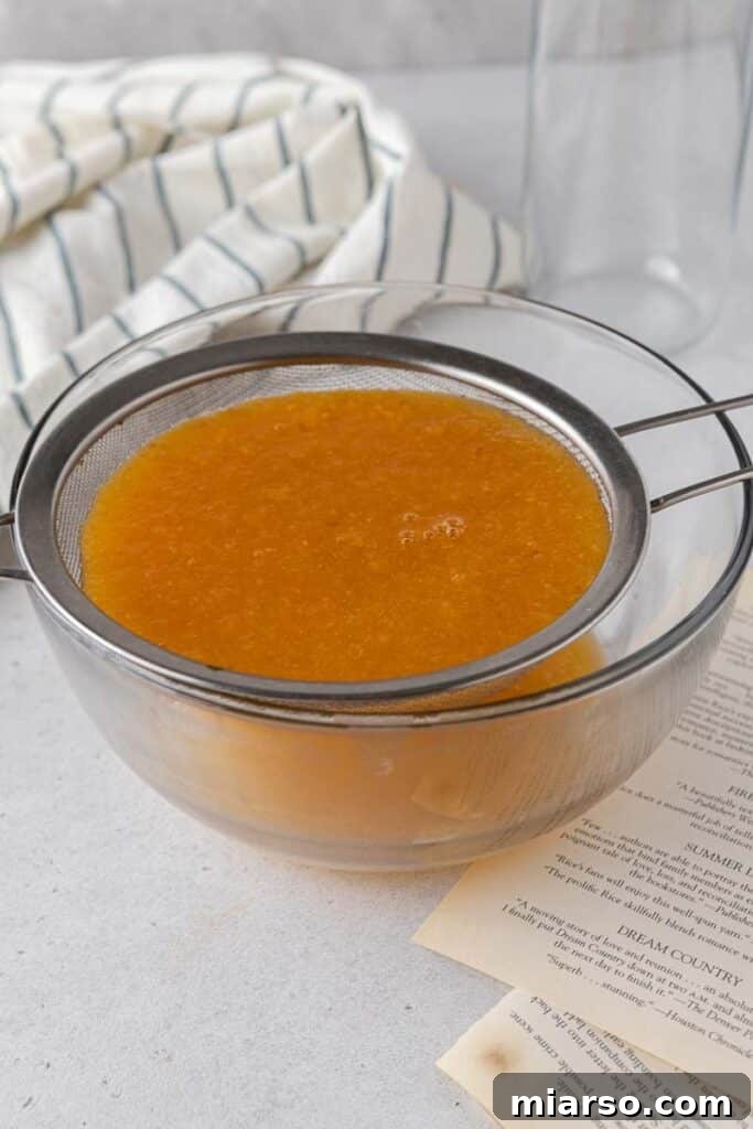 Straining the cooked peach puree through a fine sieve to create a smooth, clear peach syrup.