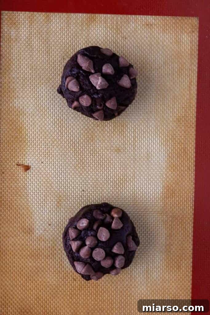 Double chocolate cookie dough balls topped with chocolate chips on a baking mat.