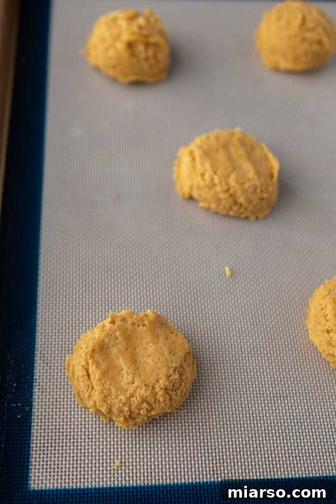 Scooped pumpkin cookie dough balls arranged on a parchment-lined baking sheet.