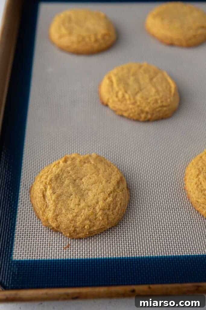 Freshly baked pumpkin cookies cooling on a baking sheet.