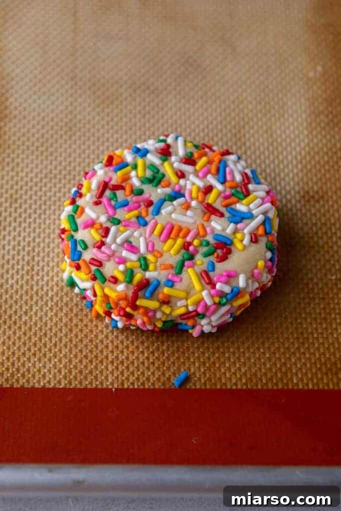 Cookie dough balls rolled in colorful sprinkles, ready for baking.