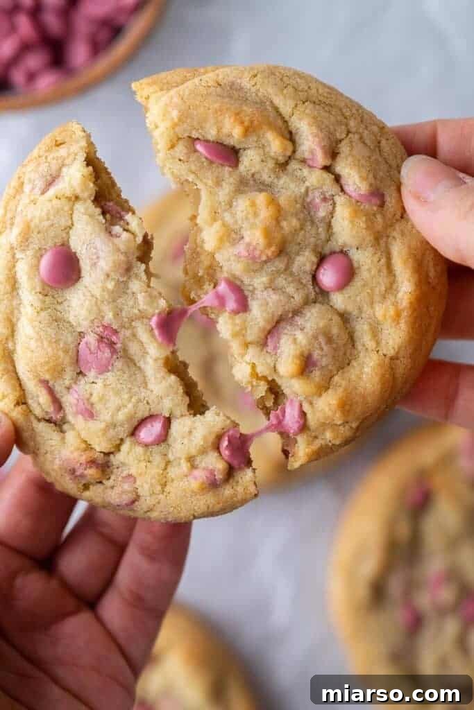 Hand breaking a ruby chocolate cookie in half, revealing its chewy interior and melted chocolate chips