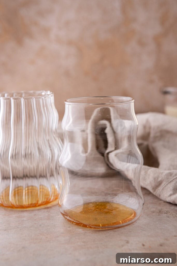 The first step in making an iced honey oat milk latte, showing rich liquid honey at the bottom of a clear glass before other ingredients are added.
