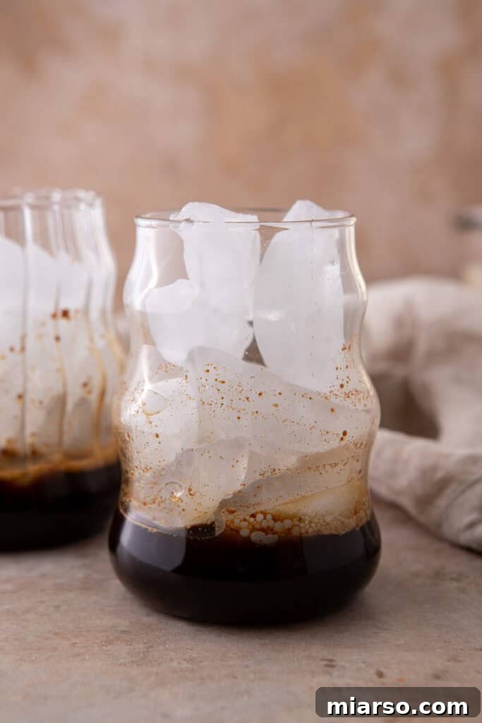 A clear glass with a dark layer of espresso poured over ice, forming the foundational layer for a refreshing iced honey oat milk latte.