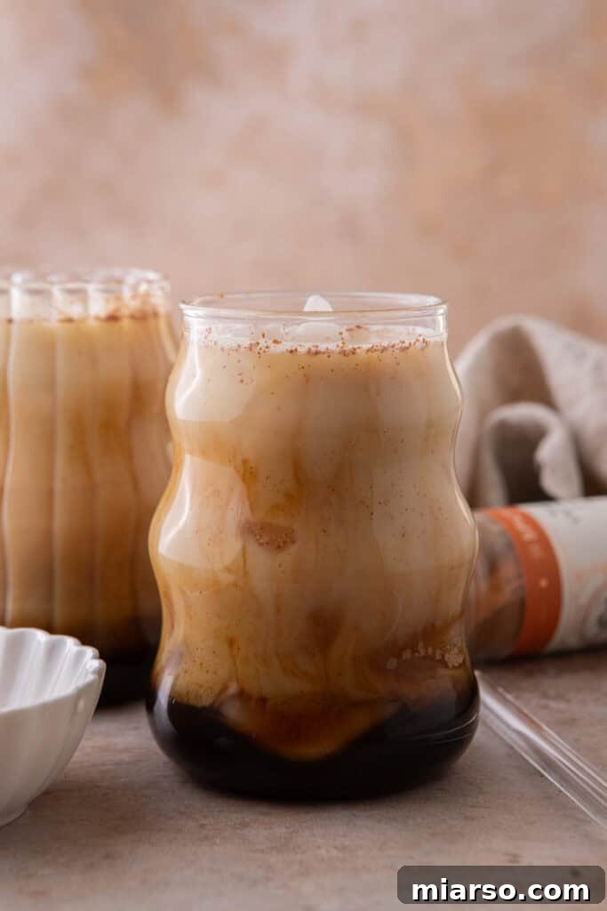 A beautifully layered creamy iced honey oat milk latte in a clear glass, with espresso and oat milk swirling together, topped with ice, ready to be stirred and enjoyed.