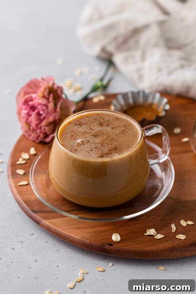 A cozy honey oat milk latte in a clear mug, garnished with cinnamon, resting on a rustic wooden tray alongside honey and oats, perfect for a relaxing morning.
