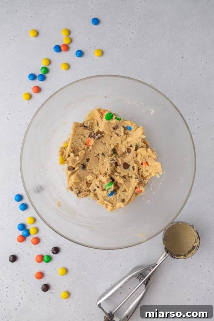 Cookie dough with M&M's, peanut butter chips, and chocolate chips mixed in a bowl.