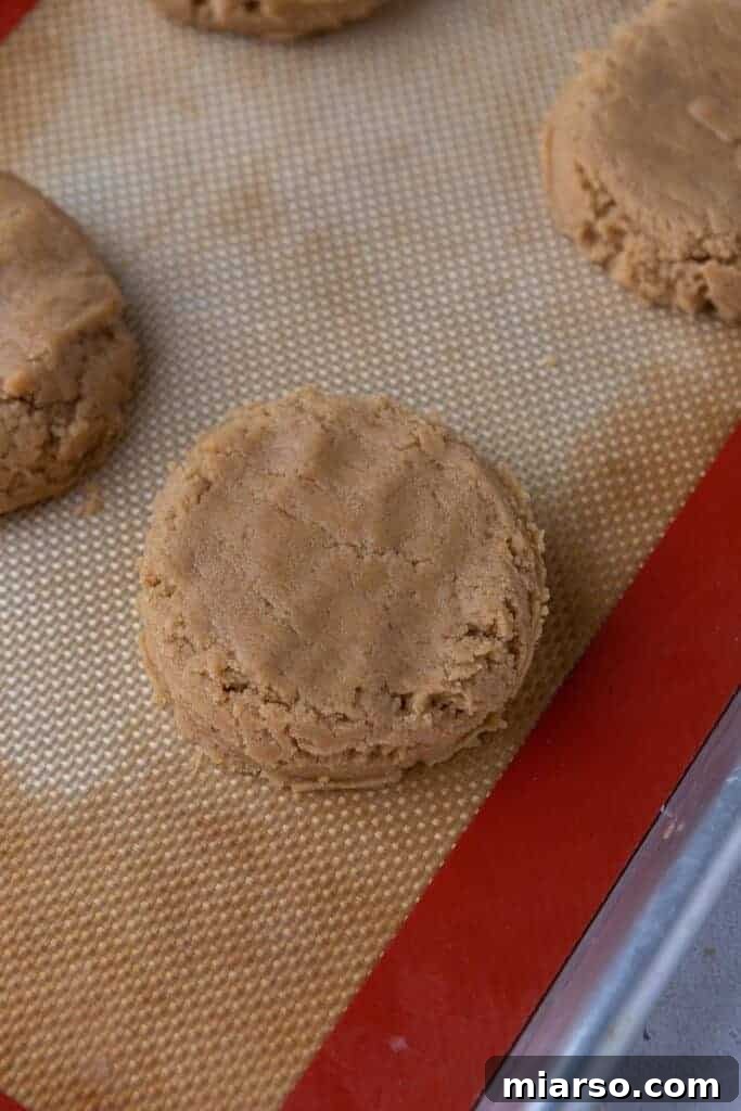 Flattened peanut butter cookie dough discs on a baking sheet.